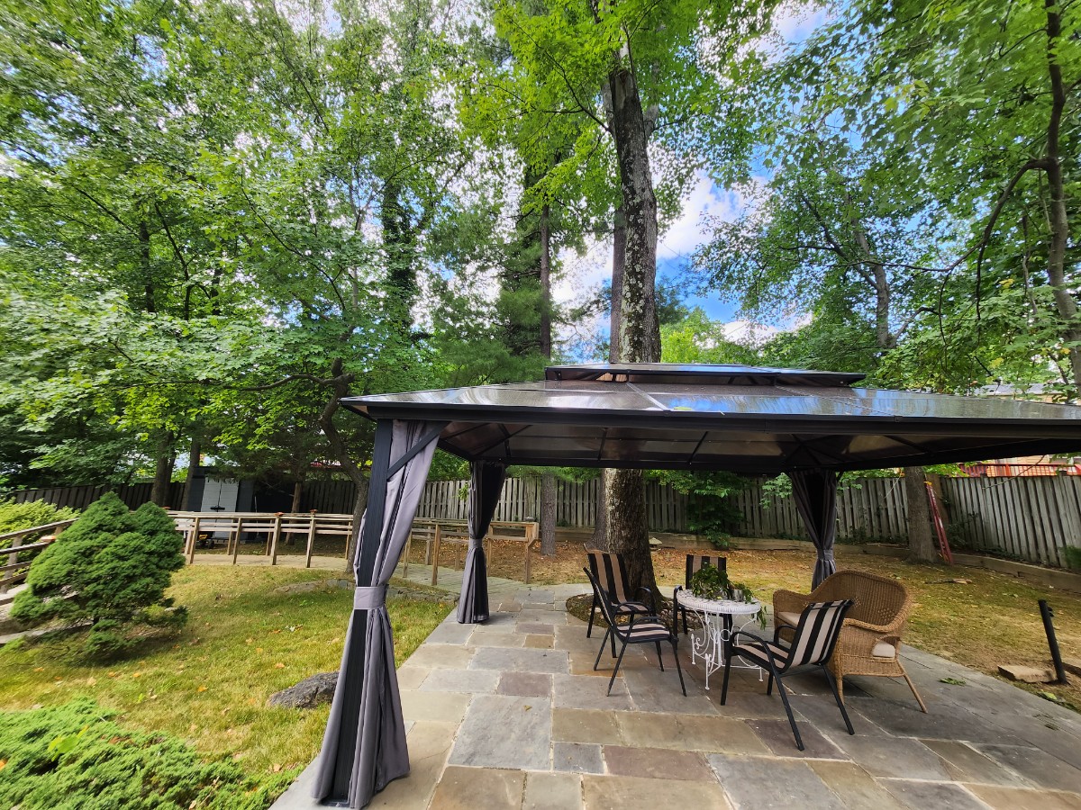 Covered gazebo seating area in the backyard, surrounded by mature trees