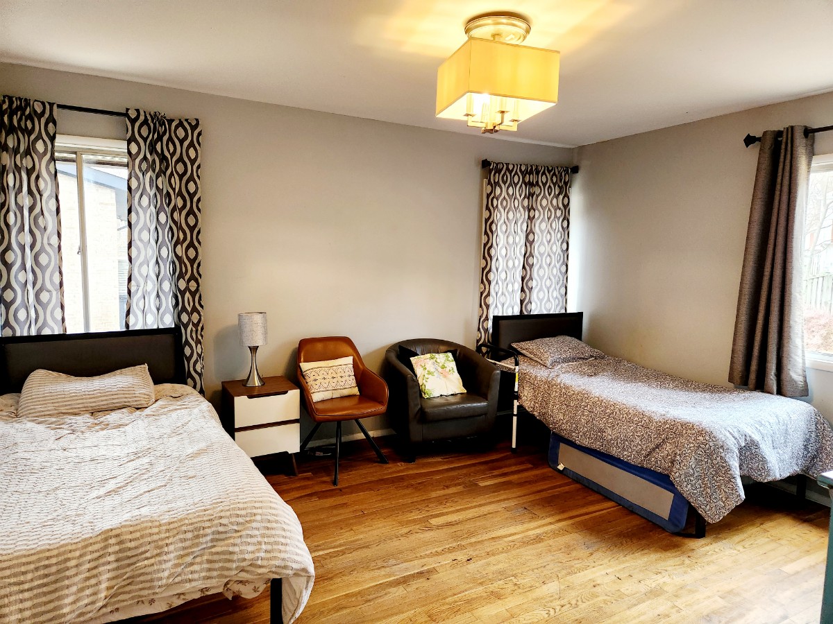 Shared Room 1 with two comfortable beds, cozy seating, and bright windows